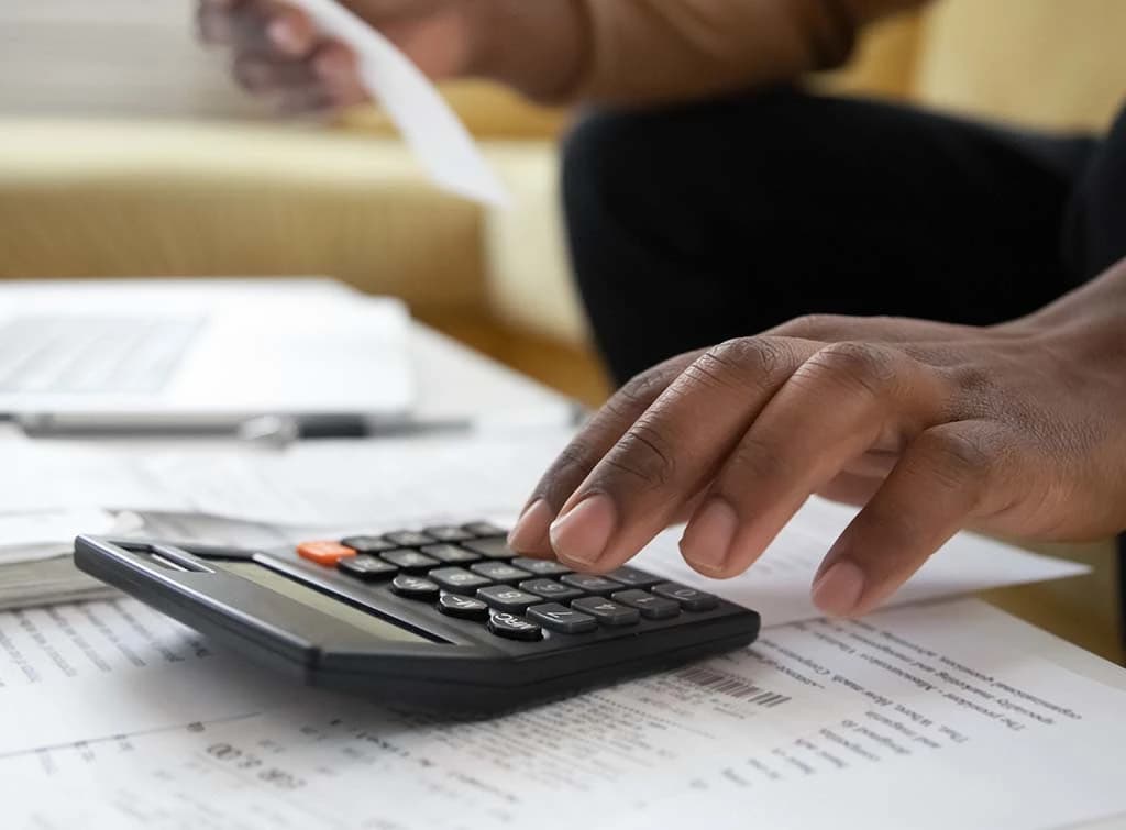 Contractor calculating invoice totals with a calculator and paperwork